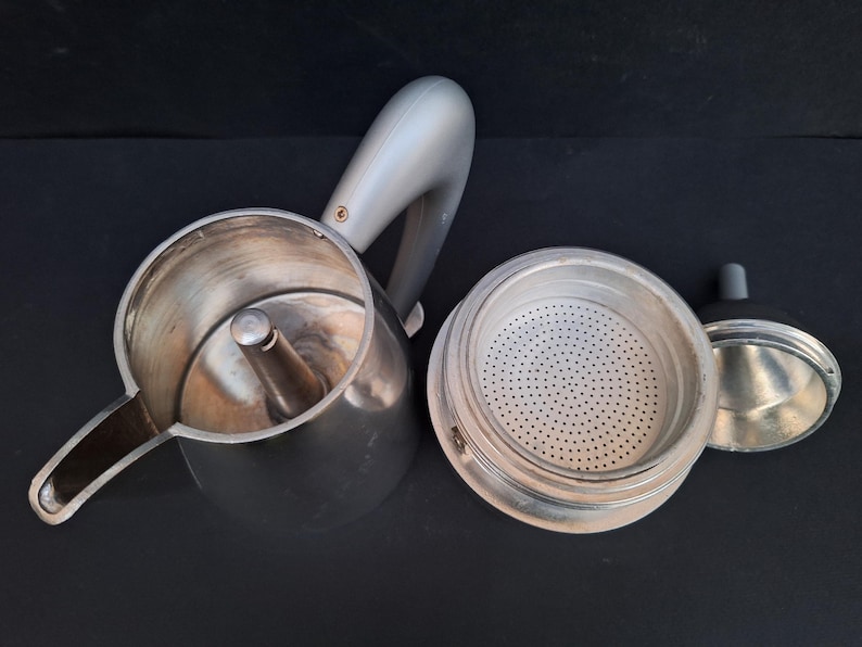 May include: A silver and gray stovetop espresso maker with a removable filter basket. The maker has a handle and a spout for pouring coffee.