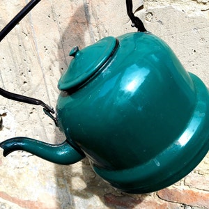 May include: A teal blue enamel teapot with a black metal handle hanging on a wall.