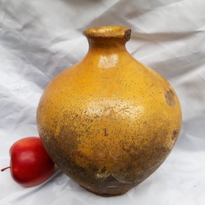 May include: A large, yellow ceramic jar with a wide mouth and a rounded body. The jar has a rustic, aged appearance with a mottled surface.