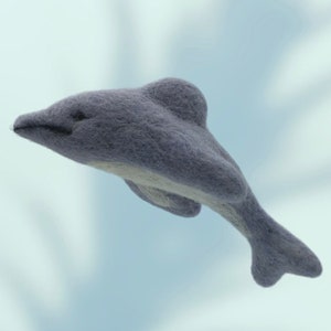 May include: A gray felt dolphin with a white belly, leaping through the air. The dolphin is a handmade toy.