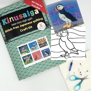 May include: A Kinusaiga stitch-free Japanese quilting craft kit featuring a blue and yellow wave pattern cover, a puffin illustration, a black and white line drawing of a puffin, a blue-handled craft tool, small pins, and blue-handled scissors.