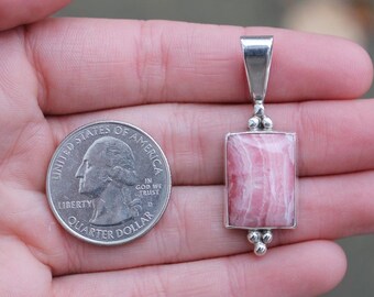May include: A silver pendant with a pink and white rectangular stone. The pendant is about the size of a US quarter.