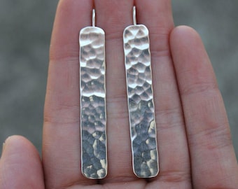 May include: A pair of silver hammered bar earrings. The earrings are long and rectangular in shape.