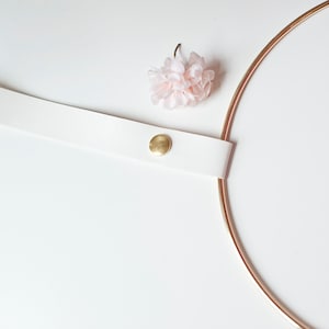 May include: A white leather strap with a gold button, a pink fabric flower, and a gold metal hoop.
