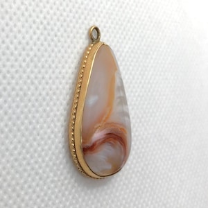 Peut inclure: Un pendentif en forme de larme avec une bordure dor&eacute;e et une pierre d'agate blanche, brune et orange.
