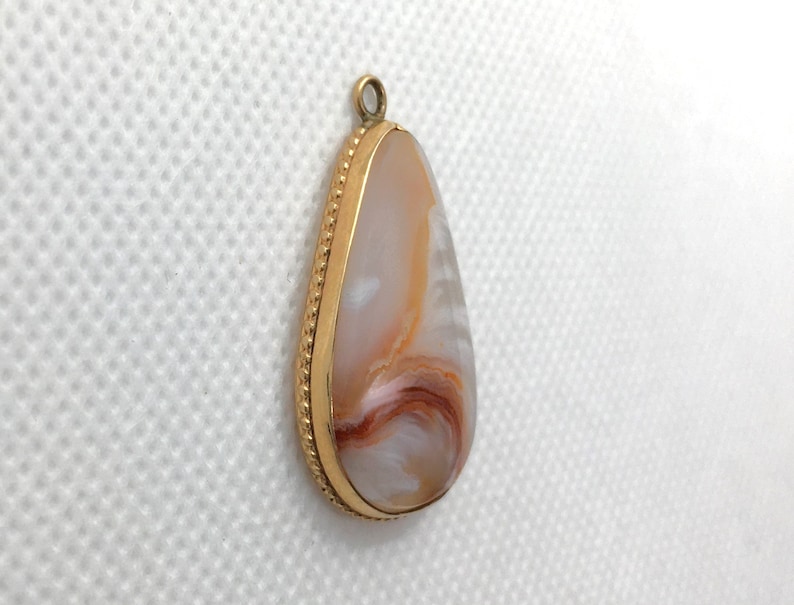 Peut inclure: Un pendentif en forme de larme avec une bordure dor&eacute;e et une pierre d'agate blanche, brune et orange.