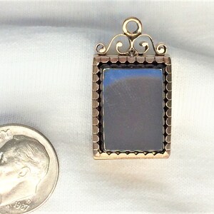 May include: A gold locket with a black cameo set in a gold frame. The locket has a decorative bail with a scroll design.
