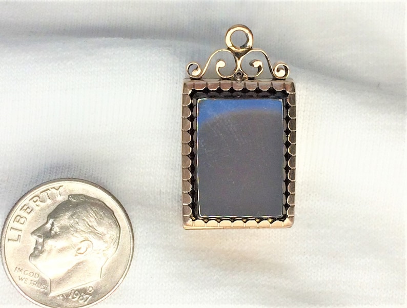 May include: A gold locket with a black cameo set in a gold frame. The locket has a decorative bail with a scroll design.