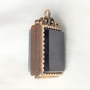May include: A gold locket with a black stone set in a scalloped frame. The locket has a decorative bail with a scroll design.