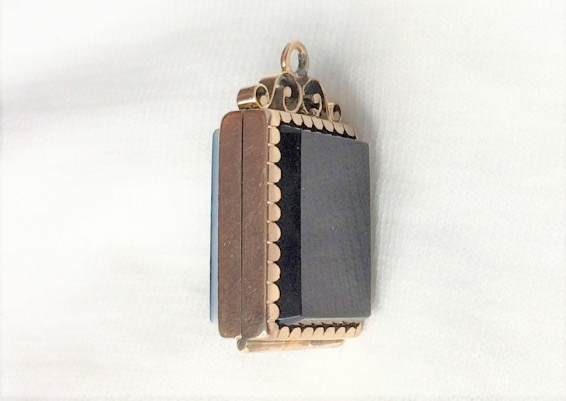 May include: A gold locket with a black stone set in a scalloped frame. The locket has a decorative bail with a scroll design.
