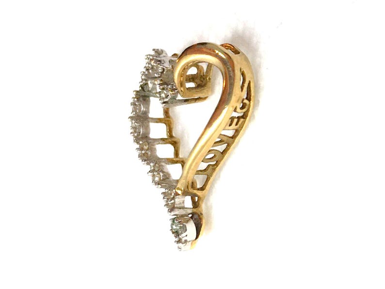 May include: Gold heart-shaped pendant with a diamond-encrusted border and the word "LOVE" inscribed on the side.