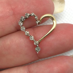 May include: A gold heart-shaped pendant with a row of small diamonds around the edge. The pendant is on a white background.