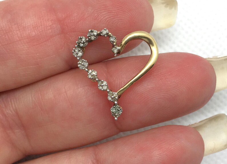 May include: A gold heart-shaped pendant with a row of small diamonds around the edge. The pendant is on a white background.