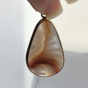 Peut inclure: Un pendentif en forme de larme avec un cadre en m&eacute;tal dor&eacute; et une pierre d'agate blanche et brune.