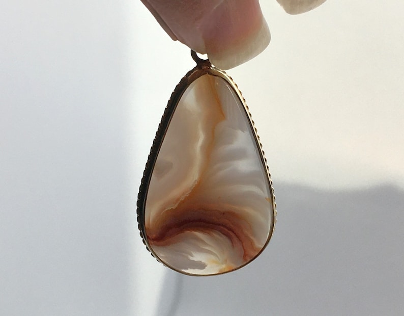 Peut inclure: Un pendentif en forme de larme avec un cadre en m&eacute;tal dor&eacute; et une pierre d'agate blanche et brune.
