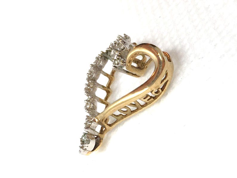 May include: A gold heart-shaped pendant with a diamond-encrusted border. The pendant has the word "LOVE" inscribed on the back.