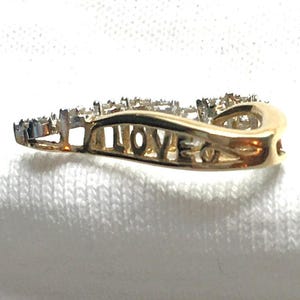 May include: A gold ring with a wave design and small diamonds set in the band. The word "LOVE" is engraved on the inside of the ring.