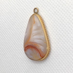 Peut inclure: Un pendentif en forme de larme avec une bordure dor&eacute;e et une pierre d'agate blanche et orange.