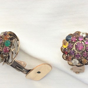 May include: A pair of gold-tone clip-on earrings featuring a cluster of colourful gemstones. The earrings include a variety of stones, such as pink, red, green, blue, and yellow.