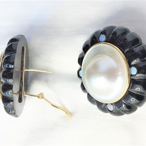 May include: A pair of black onyx and pearl earrings with gold accents. The earrings feature a large, round pearl surrounded by a black onyx setting with small, colorful gemstones.