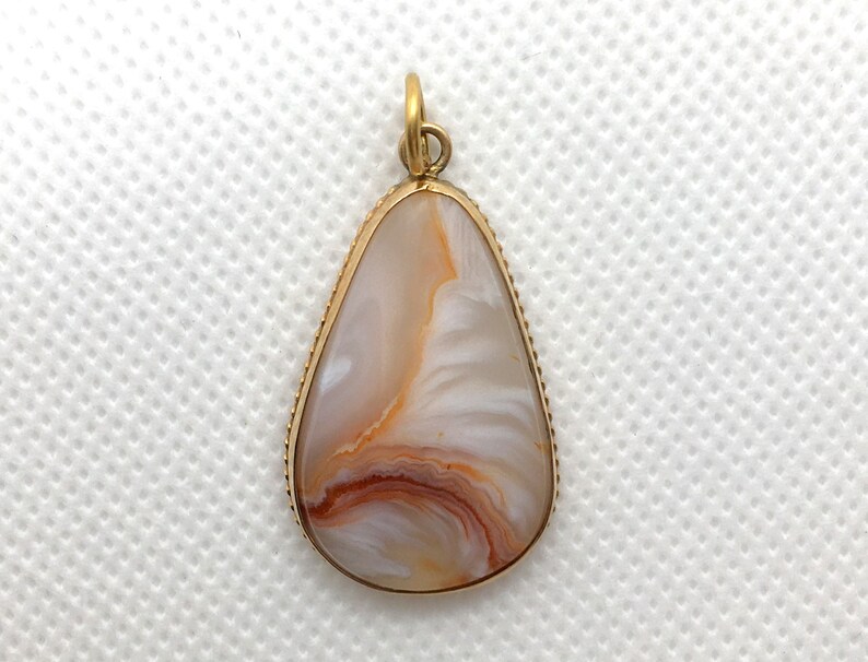 Peut inclure: Un pendentif en forme de larme avec un sertissage dor&eacute; et une pierre d'agate blanche et brune.