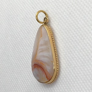 Peut inclure: Un pendentif en forme de larme avec une bordure dor&eacute;e et une pierre d'agate blanche et orange.