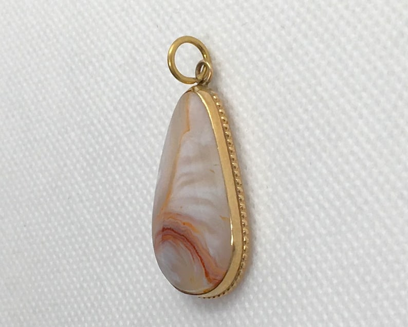 Peut inclure: Un pendentif en forme de larme avec une bordure dor&eacute;e et une pierre d'agate blanche et orange.