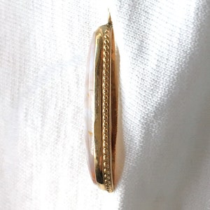 Peut inclure: Un pendentif en or avec une pierre ovale blanche et brune sertie dans un cadre en or. Le cadre est orn&eacute; d'une bordure d&eacute;corative en or.