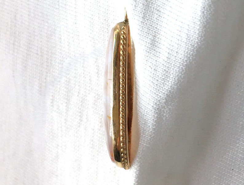 Peut inclure: Un pendentif en or avec une pierre ovale blanche et brune sertie dans un cadre en or. Le cadre est orn&eacute; d'une bordure d&eacute;corative en or.