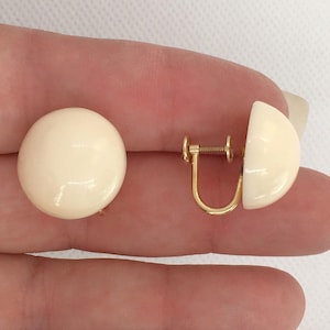 May include: A pair of cream-colored clip-on earrings with gold-tone metal clasps.