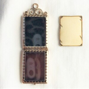 May include: A gold locket with a black and brown cameo inside. The locket is open and the cameo is visible. The locket is on a white background.