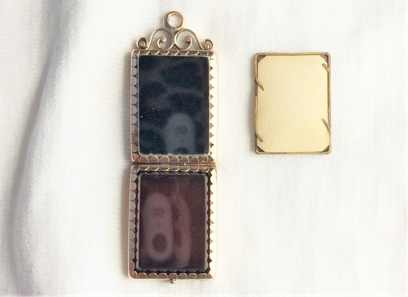 May include: A gold locket with a black and brown cameo inside. The locket is open and the cameo is visible. The locket is on a white background.