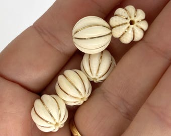 May include: Five round, off-white beads with a ribbed, pumpkin-like texture. Each bead features thin, vertical gold-colored metallic lines running between the ridges. One bead is positioned to clearly show the small, circular hole in its center.