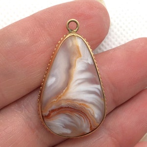 Peut inclure: Un pendentif en forme de larme avec un cadre en m&eacute;tal dor&eacute; et une pierre d'agate blanche et brune.