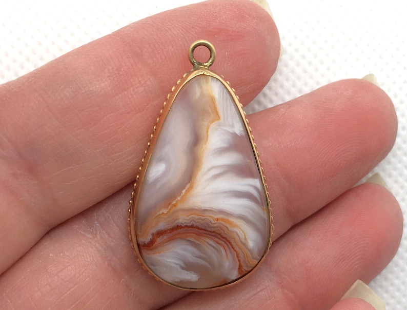 Peut inclure: Un pendentif en forme de larme avec un cadre en m&eacute;tal dor&eacute; et une pierre d'agate blanche et brune.