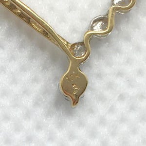 May include: Close-up of a gold heart-shaped pendant with a row of small diamonds. The pendant is marked "10K" on the back.