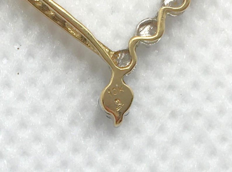 May include: Close-up of a gold heart-shaped pendant with a row of small diamonds. The pendant is marked "10K" on the back.