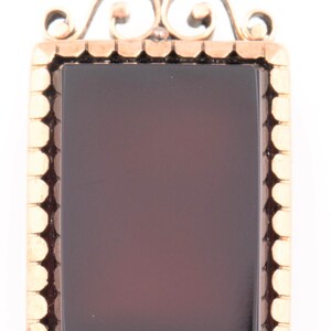 May include: A gold locket pendant with a dark red cameo set in a gold frame. The locket has a decorative bail with a scroll design.