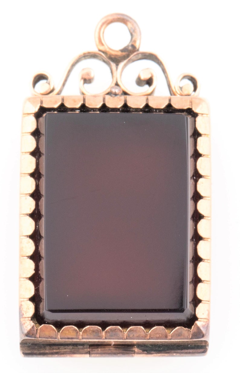 May include: A gold locket pendant with a dark red cameo set in a gold frame. The locket has a decorative bail with a scroll design.