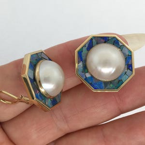 May include: Gold-tone octagonal earrings with a large white pearl center and a mosaic of blue and green stones around the pearl. The earrings have a lever back closure.