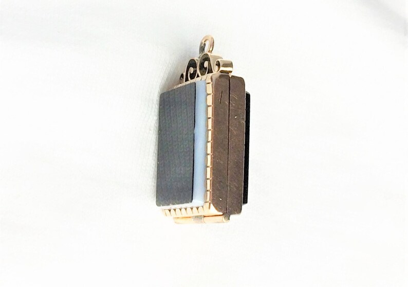 May include: A gold locket pendant with a black and white cameo. The locket has a decorative design on the top and a hinged opening.