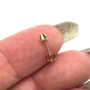 May include: A small gold stud earring featuring a tiny, round, green gemstone set in a simple metal prong setting. The earring includes a thin post and a matching gold butterfly-style friction back closure, designed for secure attachment to an earlobe.