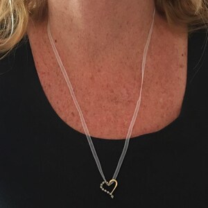 May include: A delicate heart-shaped pendant necklace with a clear ribbon chain. The pendant is made of gold and has small black accents.