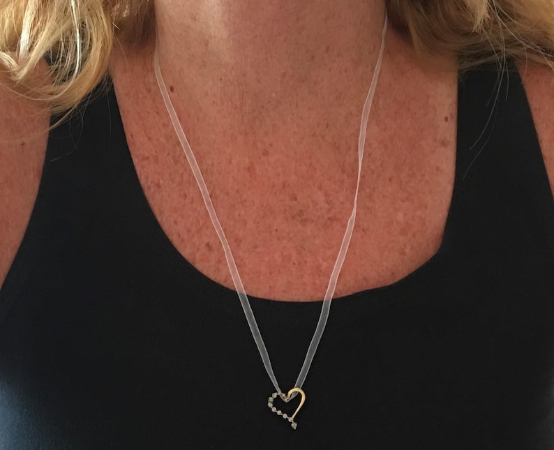 May include: A delicate heart-shaped pendant necklace with a clear ribbon chain. The pendant is made of gold and has small black accents.