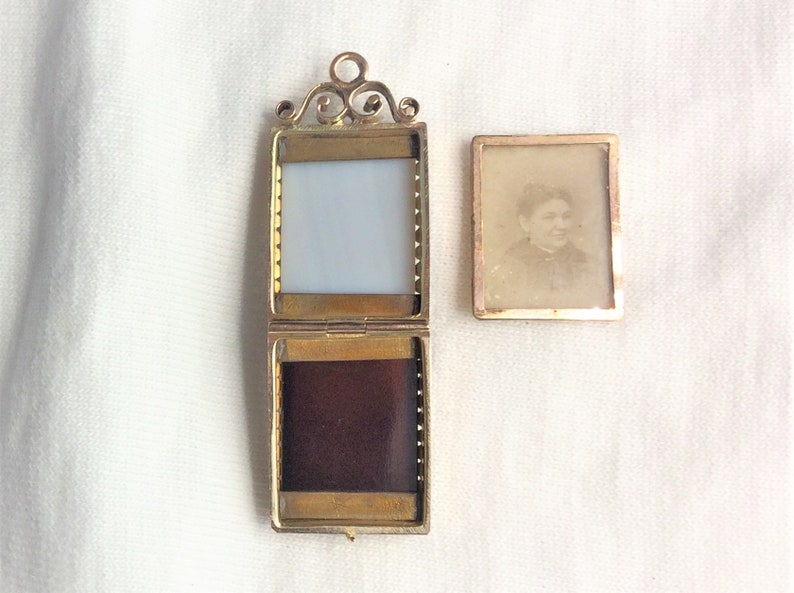 May include: A gold locket with a hinged front and back. The front has a clear glass window and the back has a dark velvet lining. The locket is open and a separate photo of a woman is visible.