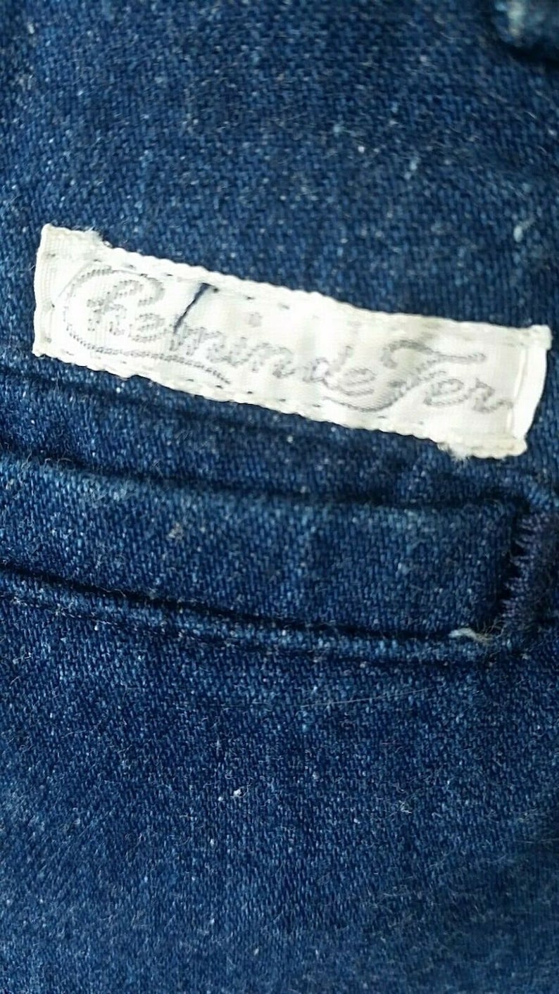 Pu&ograve; includere: Un primo piano di un tessuto denim blu con un'etichetta bianca che dice "Handmade" in corsivo.