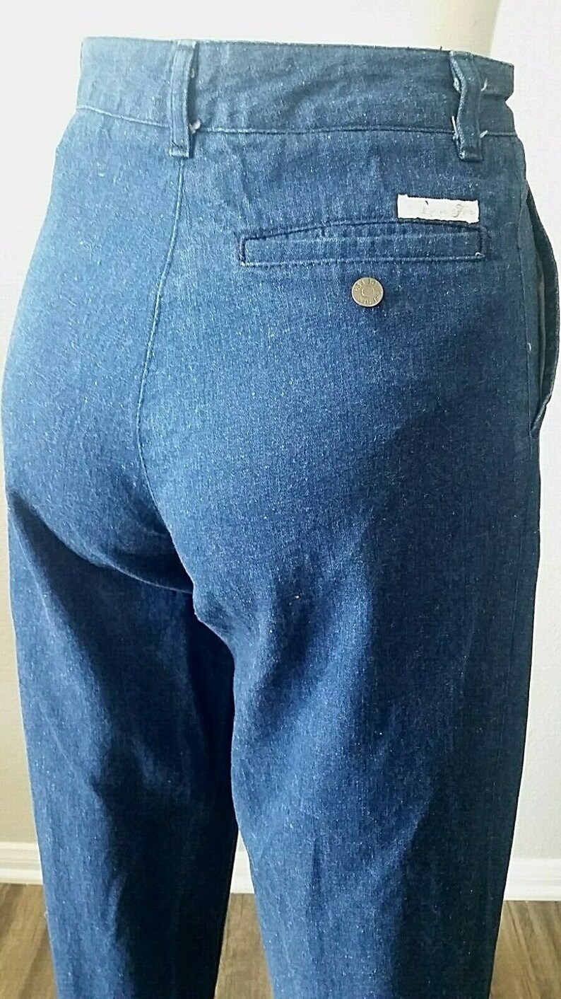 Pu&ograve; includere: Un paio di pantaloni di jeans blu scuro con una sola tasca posteriore e un piccolo bottone di metallo sulla tasca posteriore destra.