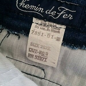 Pu&ograve; includere: Un'etichetta in denim blu con testo bianco che recita "Chemin de Fer" e istruzioni per la cura. L'etichetta include anche la taglia 28XL, il taglio 809 e il RN 51971.