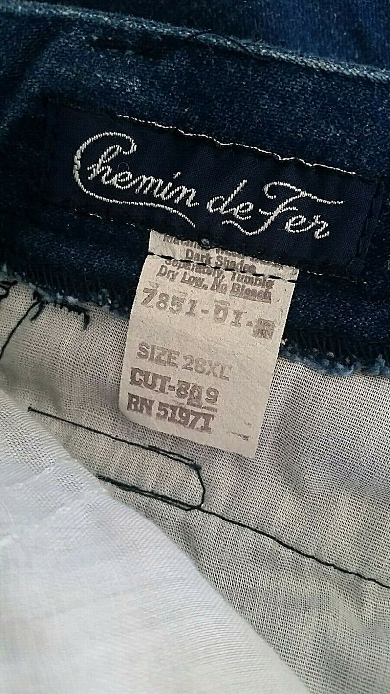 Pu&ograve; includere: Un'etichetta in denim blu con testo bianco che recita "Chemin de Fer" e istruzioni per la cura. L'etichetta include anche la taglia 28XL, il taglio 809 e il RN 51971.