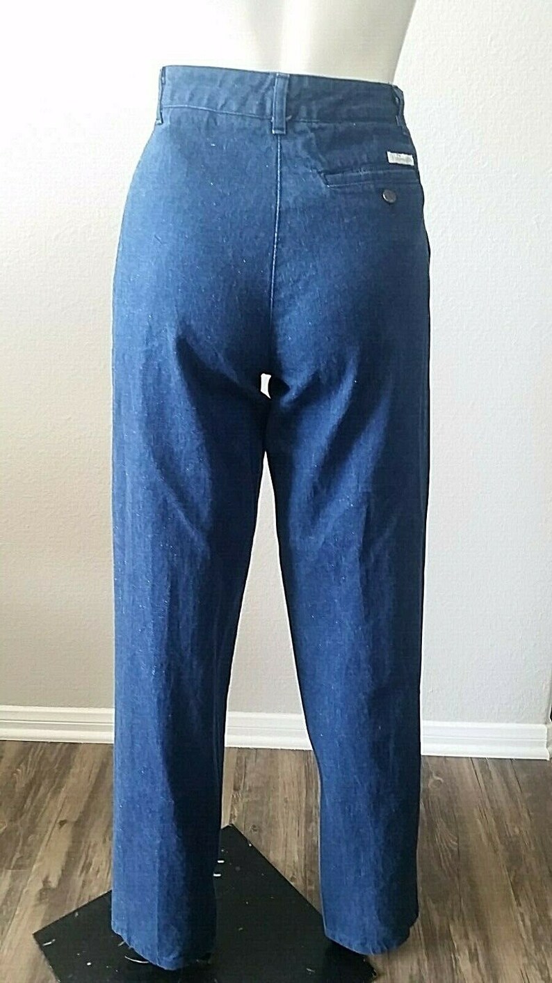 Pu&ograve; includere: Un paio di pantaloni di jeans blu scuro a gamba dritta. I pantaloni hanno una chiusura con bottoni e passanti per la cintura.